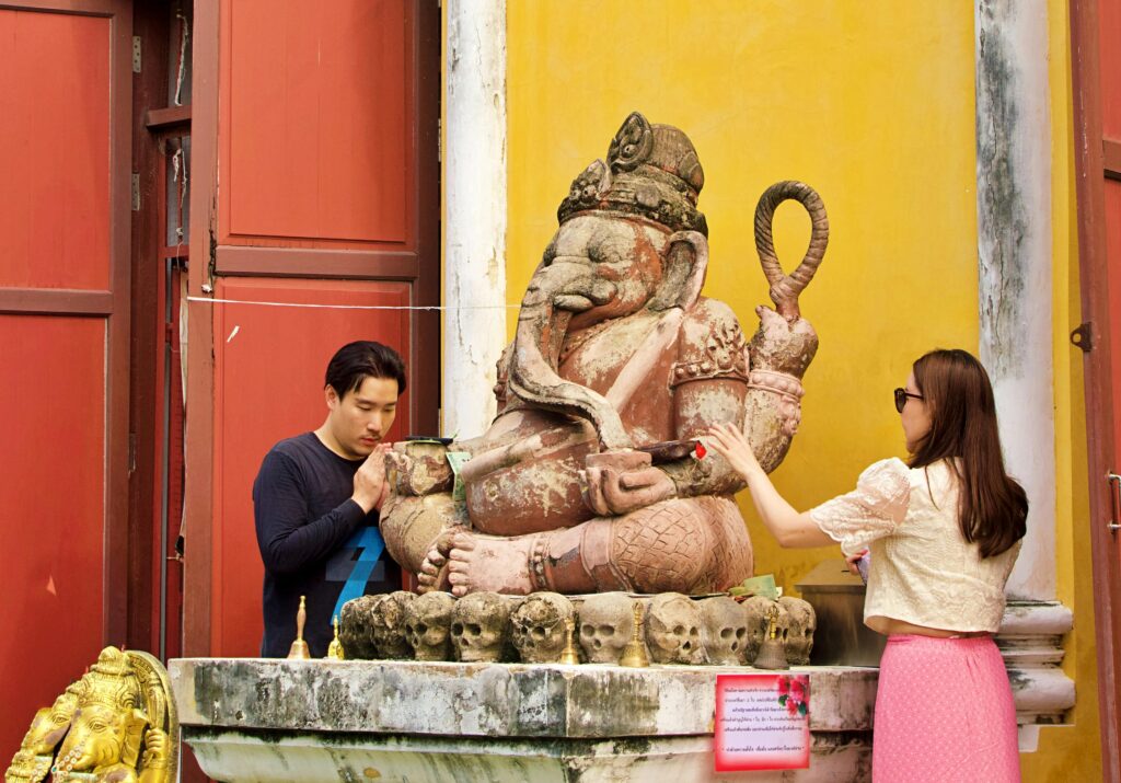 Visitors engage in worship at a Ganesha statue in Thailand, highlighting cultural reverence.